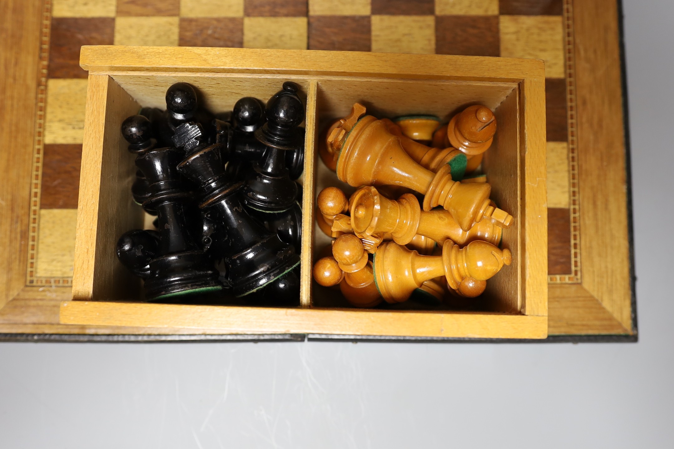 Two complete wood carved cased chess set pieces, king: 8cm and 7.5cm tall, together with a playing board